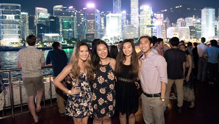 Four students pose in front of the water and cityscape of Hong Kong.