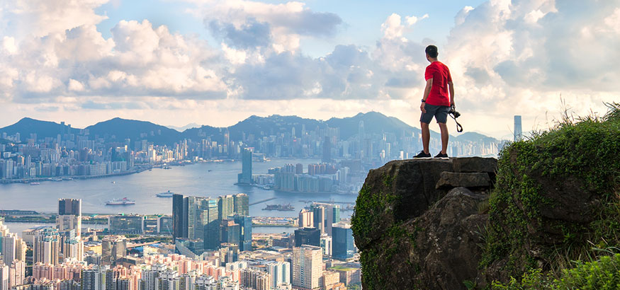 Photographer in red shirt admiring the Hong Kong skyline from above.