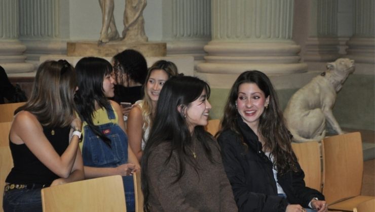 A group of seven students sitting in a museum for a presentation, marble statues in the background