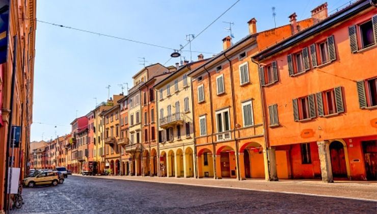 A street of orange, and yellow buildings line a cobblestone street on a partly cloudy day.