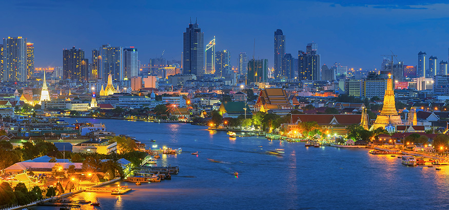The Chao Phraya River Wat Arun curves around high-rise buildings at dusk in Bangkok, Thailand..