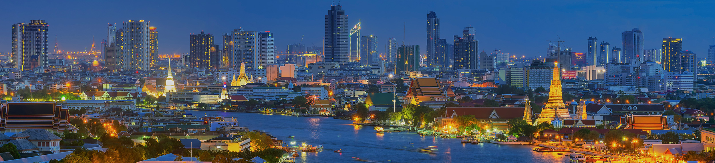 The Chao Phraya River Wat Arun curves around high-rise buildings at dusk in Bangkok, Thailand..