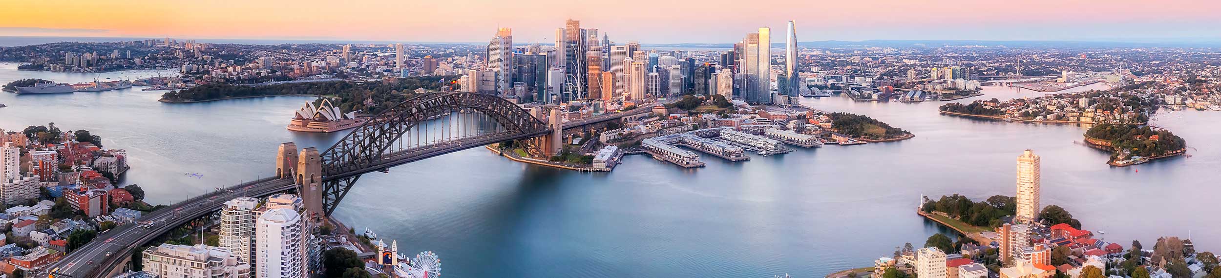 Wide aerial panorama of Sydney harbor around major city architecture landmarks.