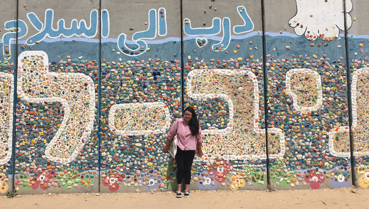 A students standing against a colorful mural with Hebrew and Arabic writings in Israel.