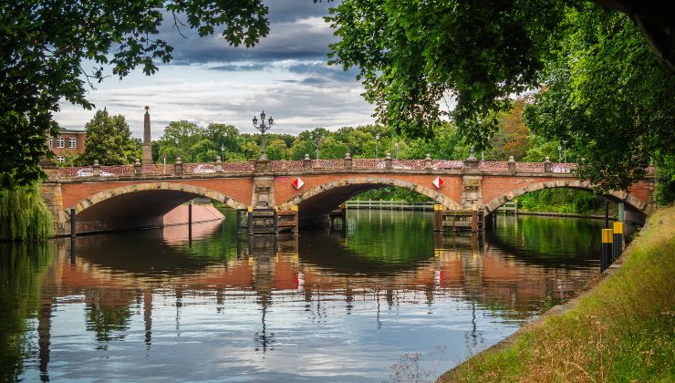 A view of a wide brown bridge made of brick sitting atop a river, surrounded by trees. 