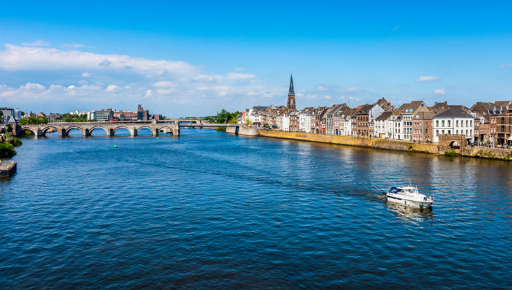 View of Maas River on a sunny day with a boat and Saint Servatius Bridge in the background in Maastricht, Netherlands.