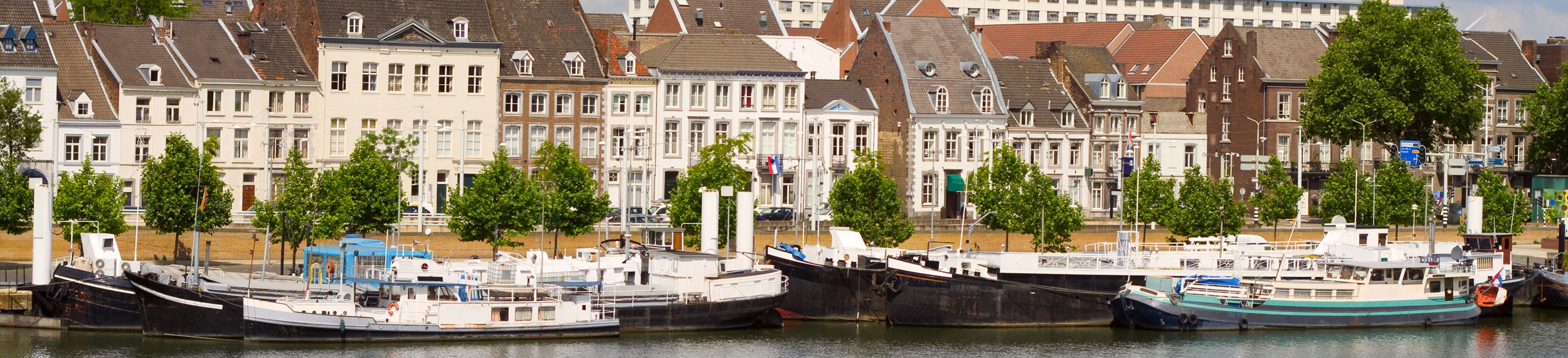 Landscape shot of buildings and boats along the Meuse River in Maastricht, Netherlands.