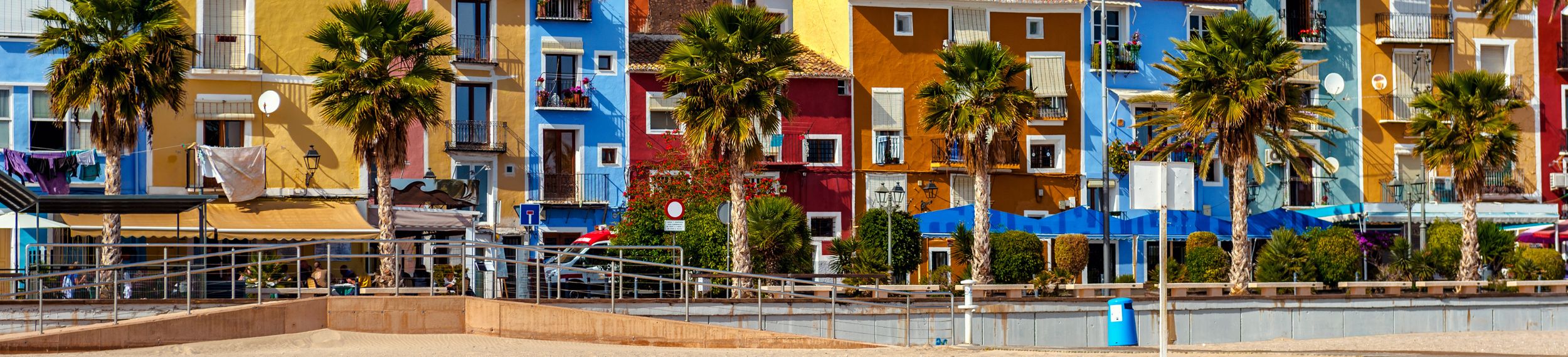 A street lined with palm trees and multicolored townhouses on the beach.