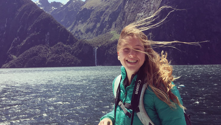 Female student smiling on a boat with a view of the water and mountains in New Zealand. 