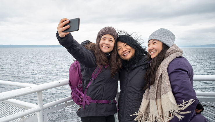 Mother and teen daughters take selfie on deck of ferry in British Columbia, Canada.