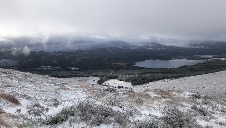 A view from a snowy hill, lake, and mountains at Cairngorm National Park.