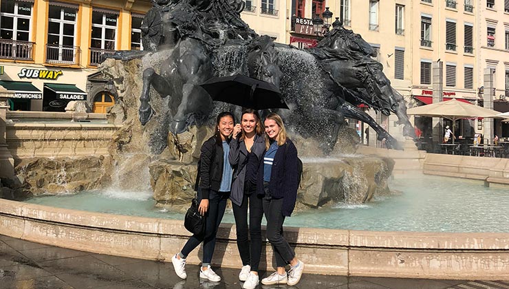 Three students standing near the Fontaine Bartholdi in Lyon, France.