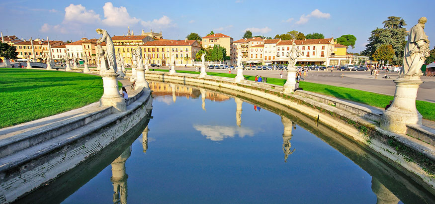 The elliptical square of Prato della Valle with a large space with a green island at the center and surrounded by a small canal bordered by two rings of statues in Padova, Italy. 