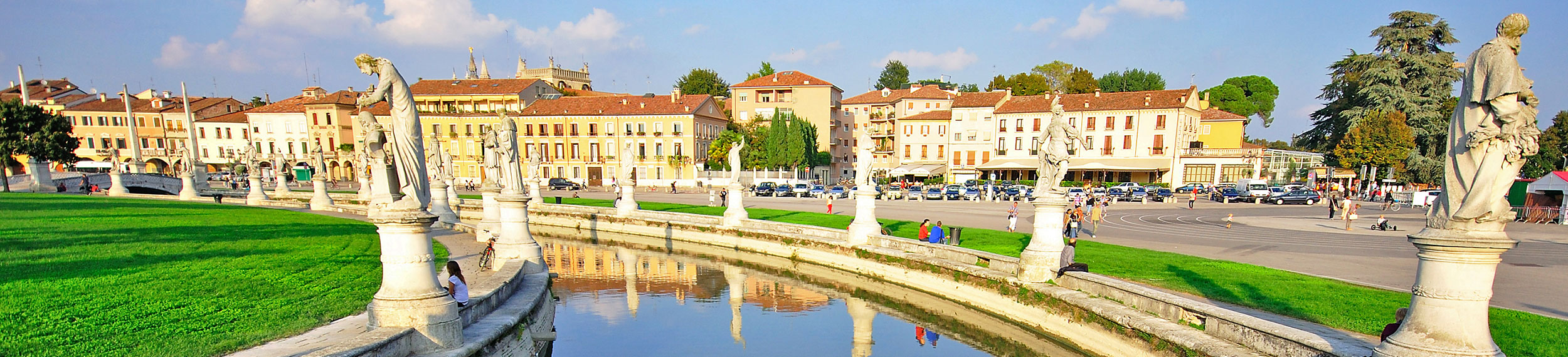 The elliptical square of Prato della Valle with a large space with a green island at the center and surrounded by a small canal bordered by two rings of statues in Padova, Italy. 