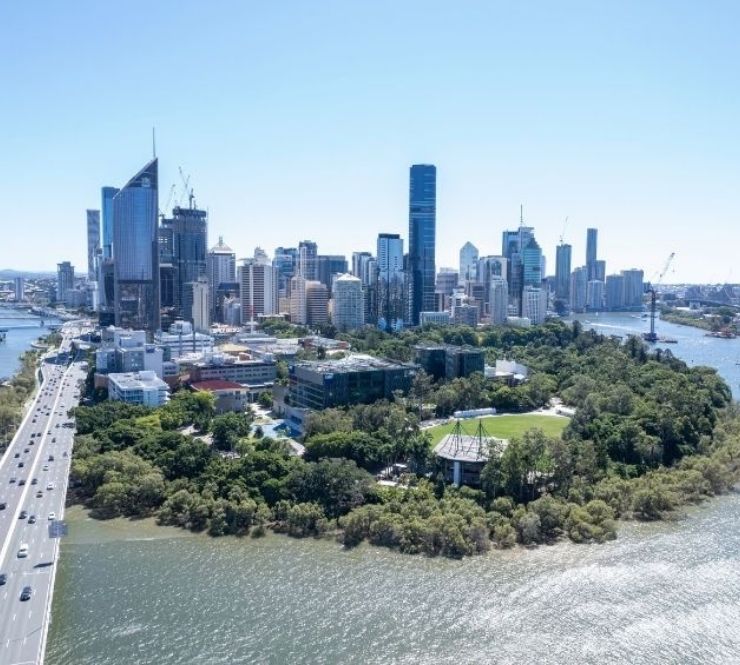 Aerial view of the Brisbane CBD from over the Brisbane River on a cloudless blue sky day with a busy bridge in the foreground and the Queensland university Garden’s Point campus in the cbd foreground