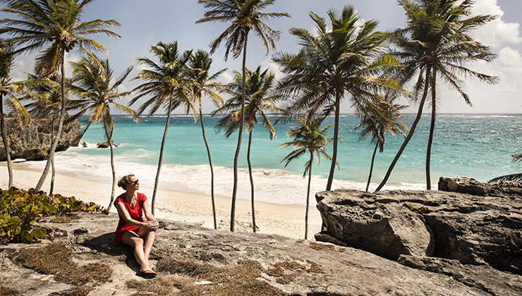 Student sits on rocks near palm trees and Bottom Bay Beach in Barbados.