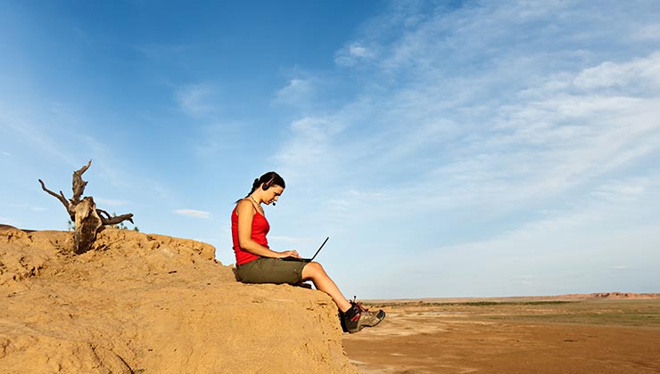 Student intern outdoors using laptop overlooking a red rock landscape, under a cloudy sky.