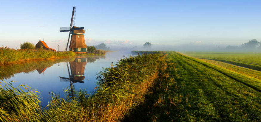 Landscape shot of windmill near a body of water and row crops in Wageningen, Netherlands. 