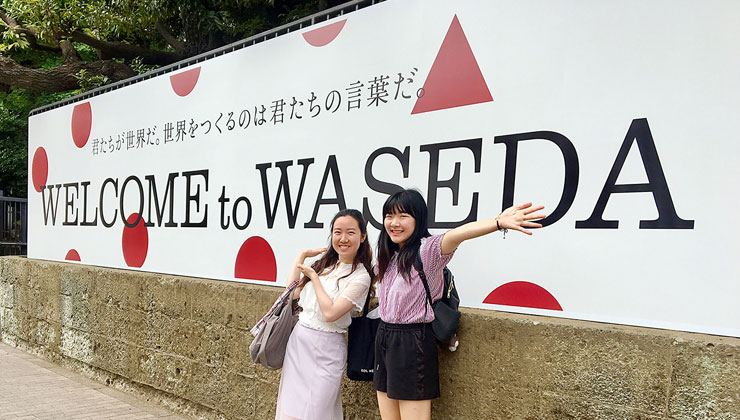 Two students smile in front of a “Welcome to Waseda” sign in Tokyo, Japan.