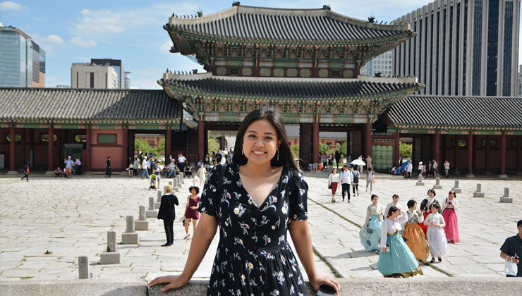 UC Los Angeles student leans against a wall and smiles in front of Gyeongbokgung Palace in Seoul, south Korea.