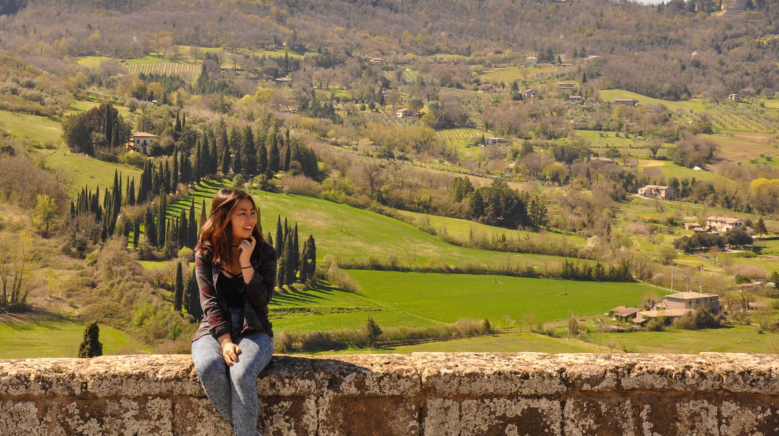 UCEAP student smiling and sitting on a ledge surrounded by greenery.