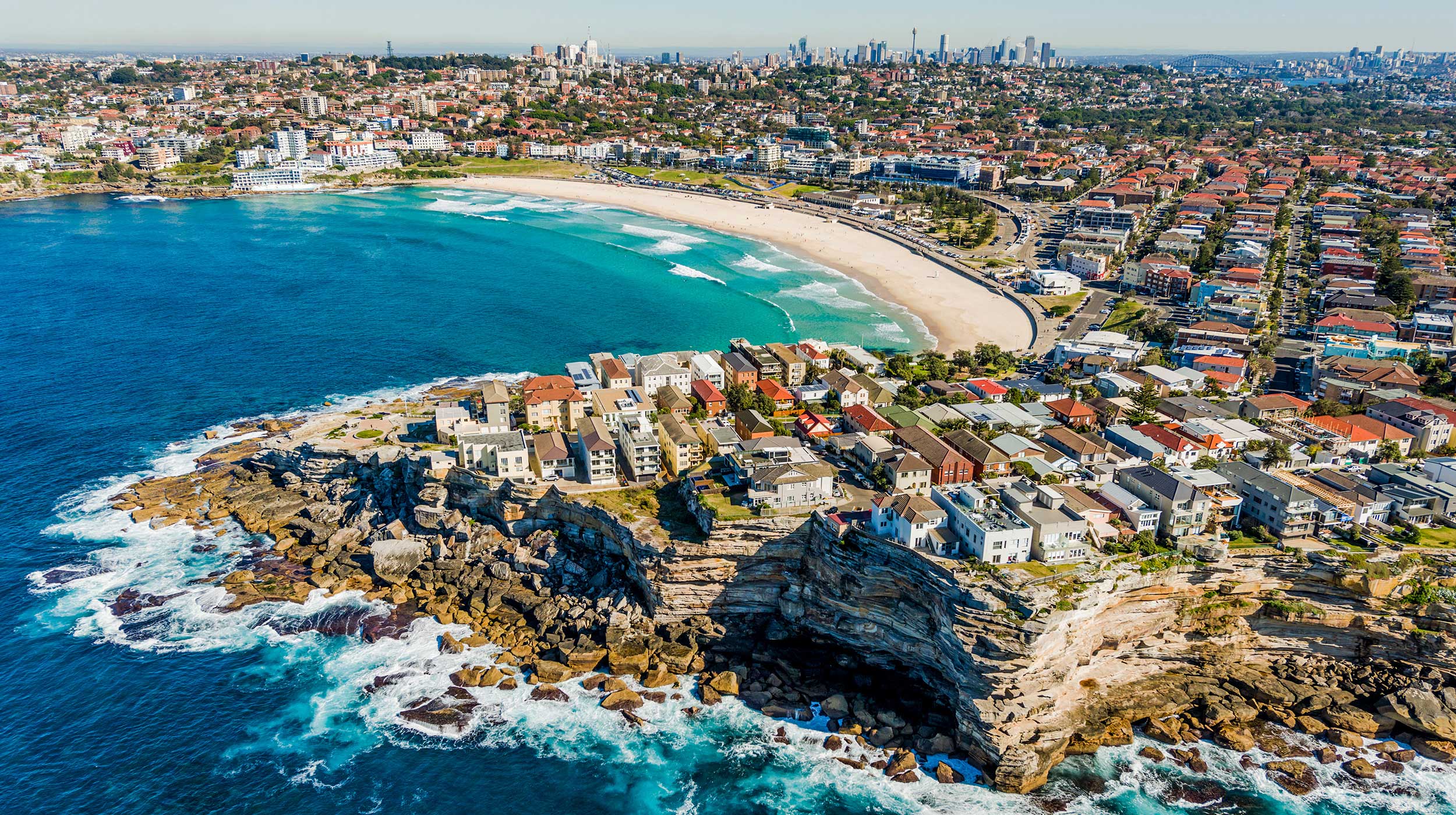 Aerial view of Bondi Beach, with Sydney skyline in background.