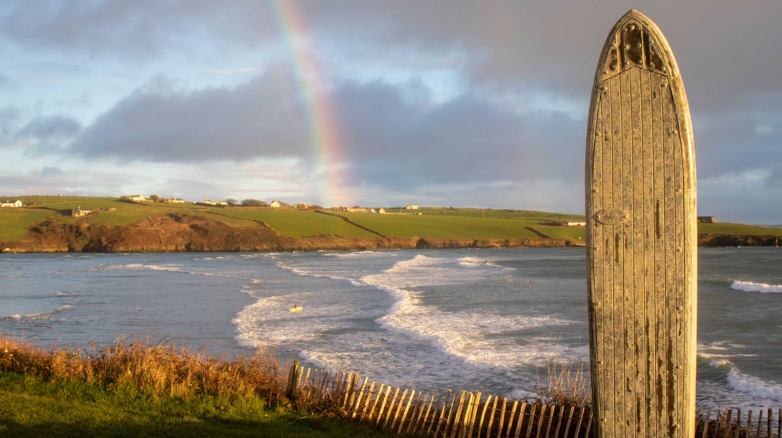 A sunset change in the weather creates a rainbow against a sandy beach at high tide in County Cork Ireland.