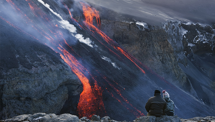 A couple watching lava flow down a mountain in Fimmvörduháls, Iceland.