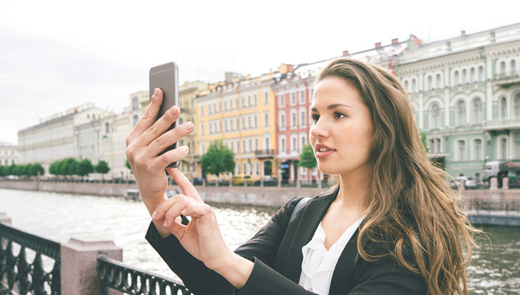 Student takes a selfie near the water and colorful buildings in Saint Petersburg, Russia.