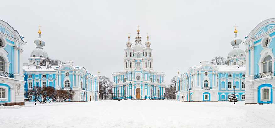 The light blue and white cathedral and surrounding buildings of Smolny Cathedral covered in snow in St. Petersburg, Russia.
