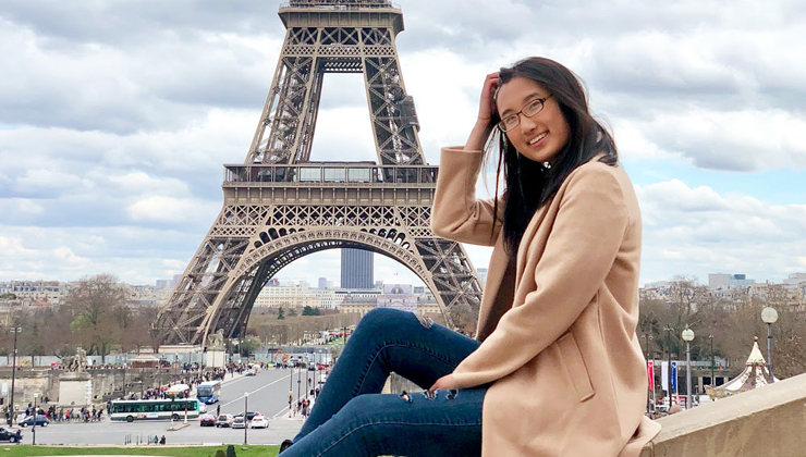A student smiling in front of the Eiffel Tower in Paris, France.