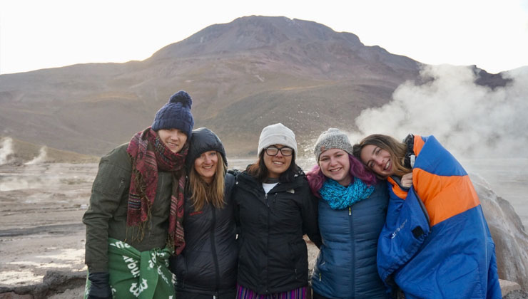 Five friends huddle together in the cold at the Geysers del Tatio in Atacama, Chile.