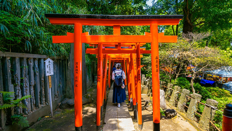 A student walks through orange columns of the Nezu Shrine on a sunny day in Tokyo, Japan. 