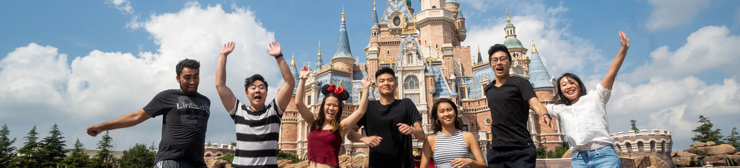 Seven friends jumping up in the air at a Disneyland park.