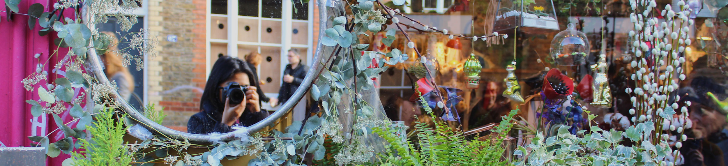 Student taking a photo of a plant display with a view of themselves in the mirror. 