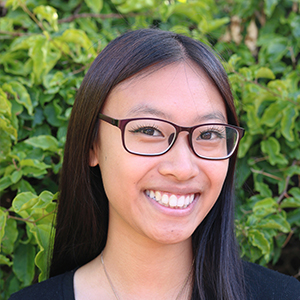Alicia Yu smile and poses for a headshot in front of greenery. 