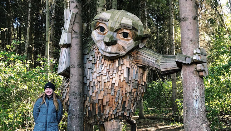 Student standing next to a giant wooden sculpture with a new friend in the woods in Copenhagen, Denmark.