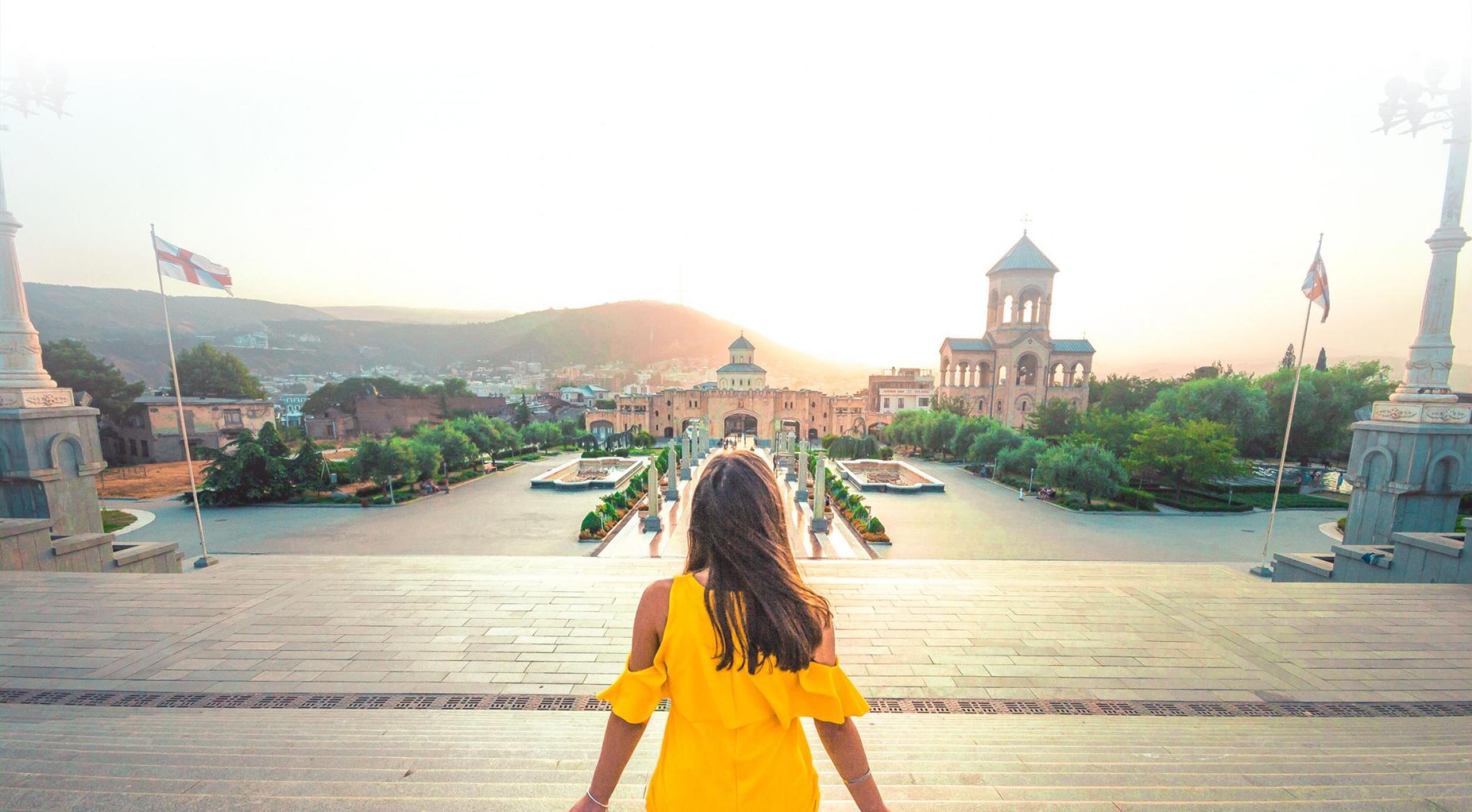 Woman in a yellow dress facing away from the camera and looking out at the cityscape.