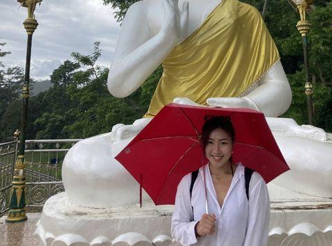 Arisa Matsuzaki with red umbrella in front of statue in Thailand