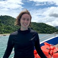 Ronnie Page-Harley smiles for a photo on a boat with a Costa Rica forest in the background. 