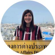 Sabrina Stone smiles for a photo holding a yellow sign featuring written Thai language.