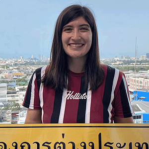 Sabrina Stone smiles for a photo holding a yellow sign featuring written Thai language.